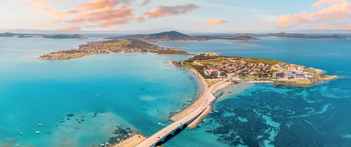 Panoramic aerial view of Cunda Island and Ayvalik, Turkiye, connected by a bridge, showcasing the vibrant turquoise Aegean Sea and coastal town