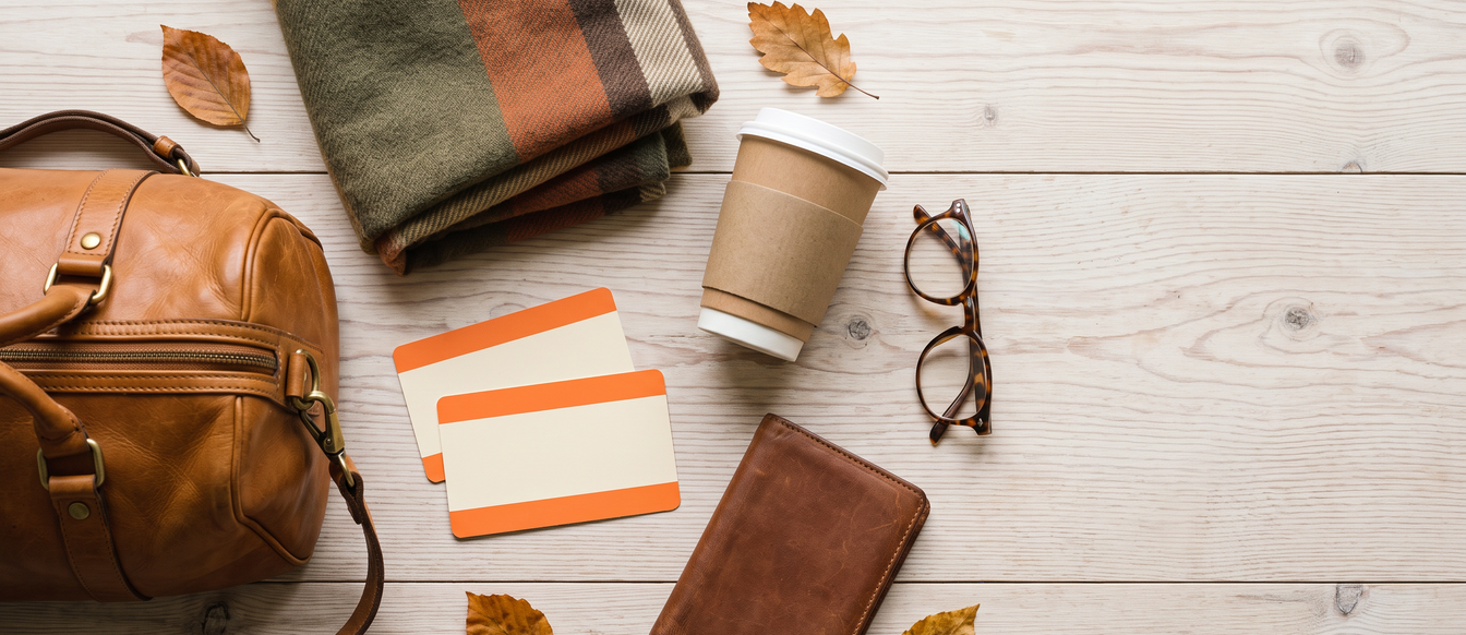 Travel flat lay with train tickets, a leather weekend bag, scarf, coffee and autumn leaves